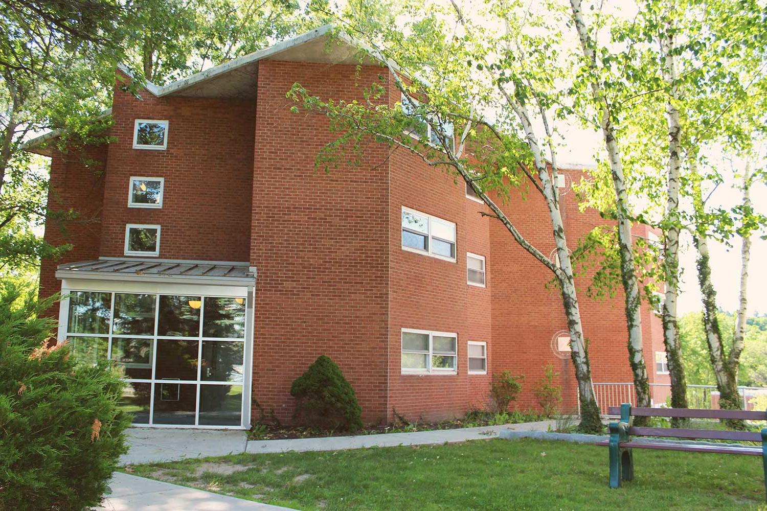 Brick res hall with windows in wooded area.